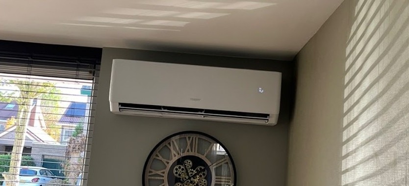Witte airco binnenunit boven een grote wandklok