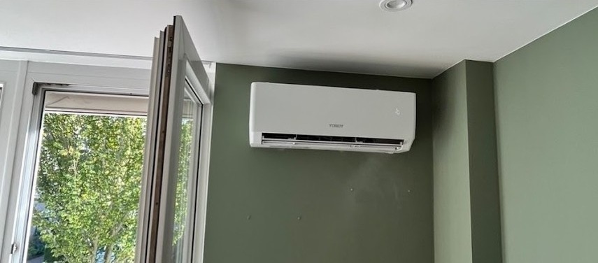 Airco binnenunit in een kamer met groene wand, naast een open raam